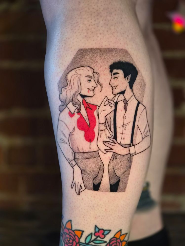 A tattoo of Louis & Lestat from the interview with a vampire tv show. They look enamoured with each other. Lestat is gently touching Louis's face, and Louis is touching his arm in turn. Lestat has blood down his chest. Their eyes are a vibrant green and blue. The border of the tattoo is coggin shaped. 