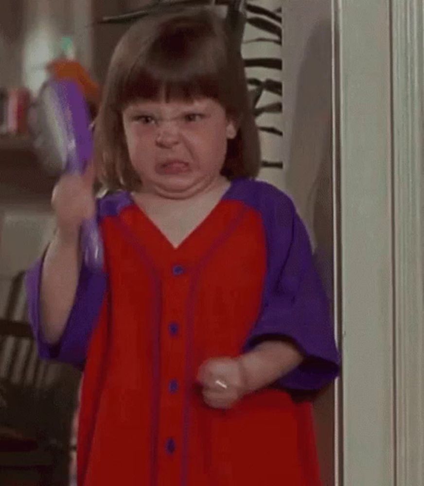 a little girl in a red and purple dress is making an angry face .