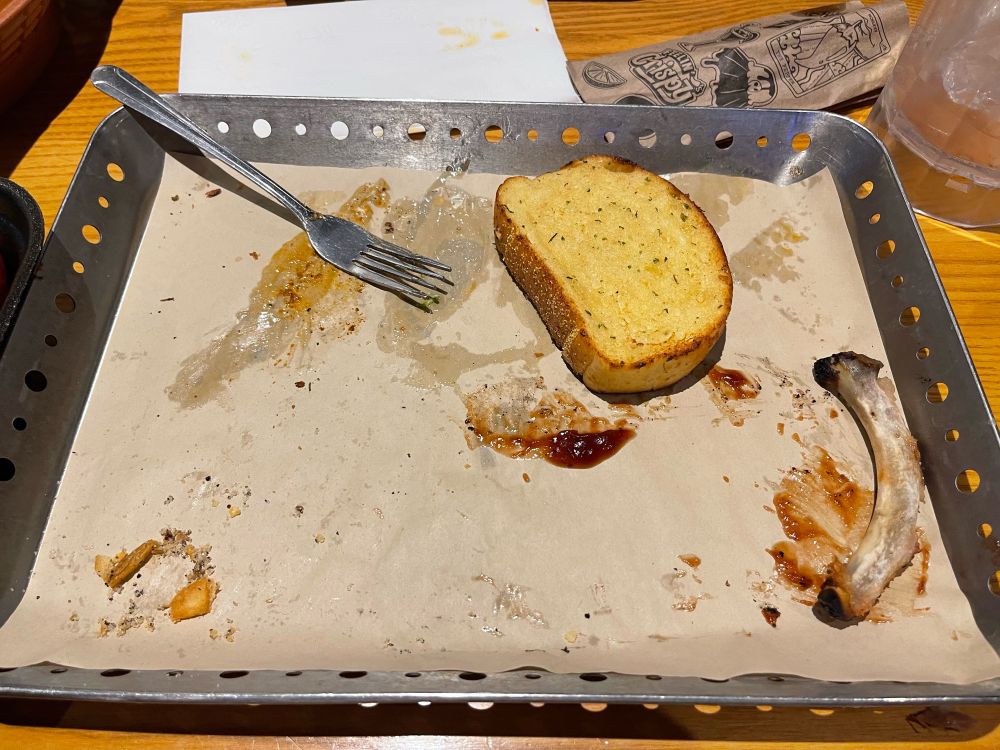 chillis tray with sauce smeared around, a fork, a piece of garlic toast, and one rib bone