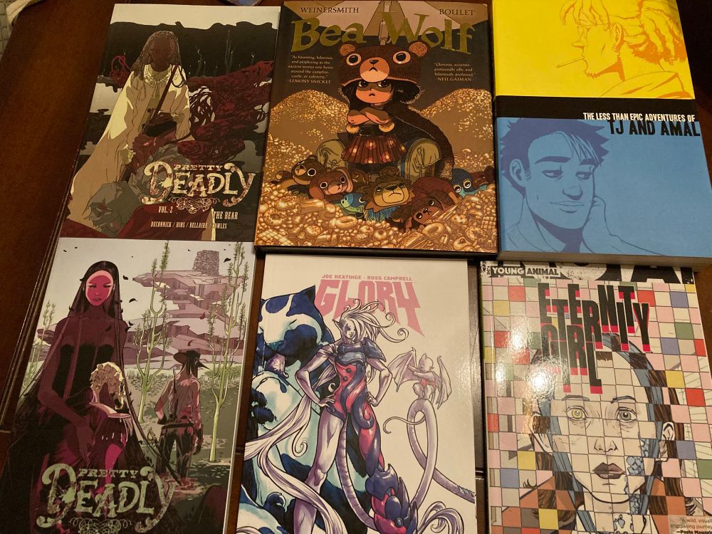 A spread of six books:
Pretty Deadly vols 1 & 2 by Kelly Sue DeConnick & Emma Rios
Bea Wolf by Zach Weinersmith & Boulet
The Less Than Epic Adventures of TJ and Amal by E.K. Weaver
Glory vol 2 by Joe Keatinge & Sophie Campbell
Eternity Girl by Magdalene Visaggio & Sonny Liew
