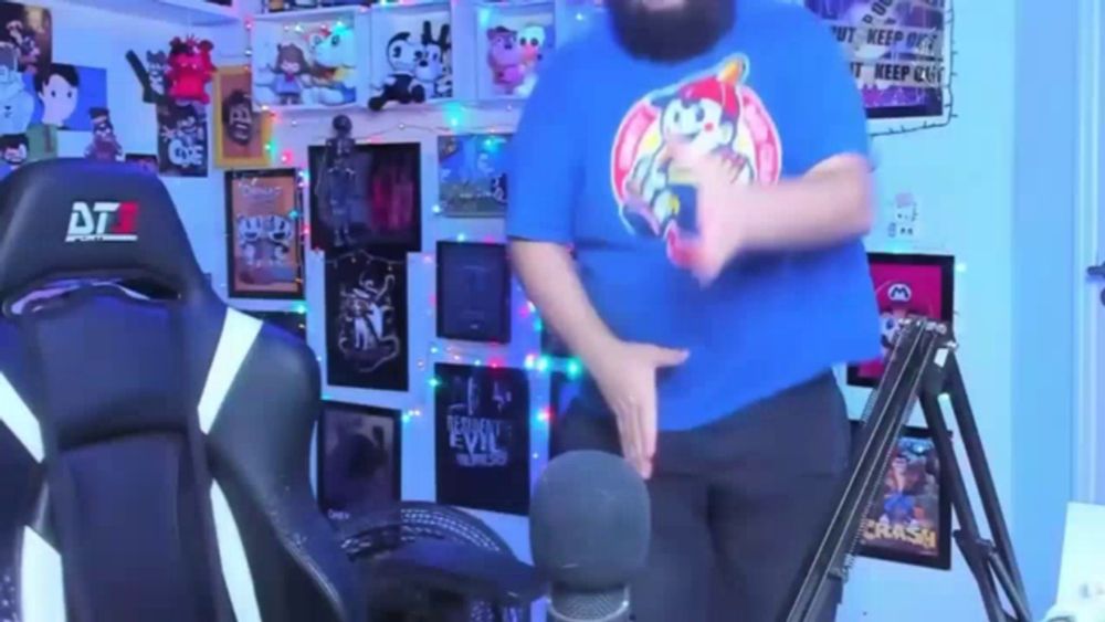 a man in a blue shirt with a sonic the hedgehog shirt on is dancing in front of a microphone .