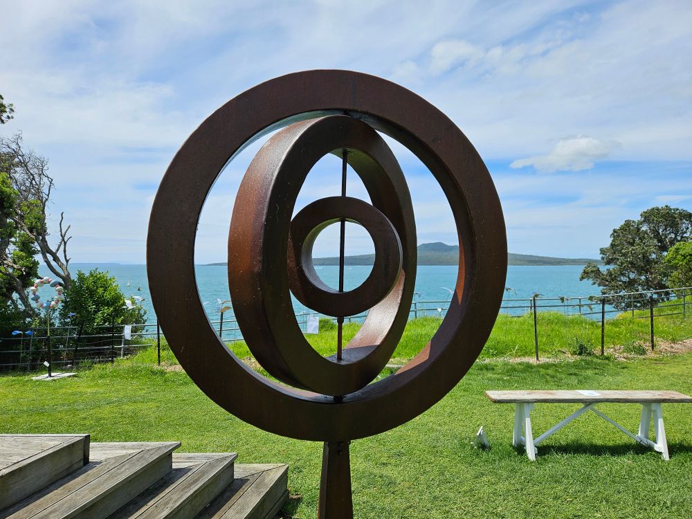 Rangitoto seen through a bronze sculpture of concentric circles set at differing angles 