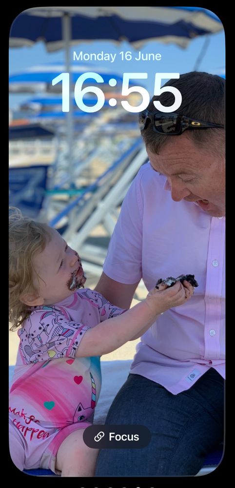 My 1 1/2 year old daughter with Oreo ice all round her face, offering me a bite, I’m wearing a spotless pink short sleeved shirt. We are sat on a beach in Viareggio, Tuscany, Italy.