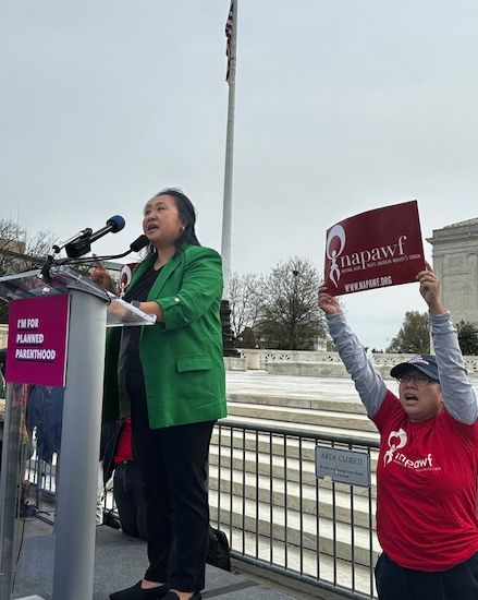 Sung Yeon Choimorrow, a Korean American woman in a green blazer, speaks to a crowd in front of the Supreme court
