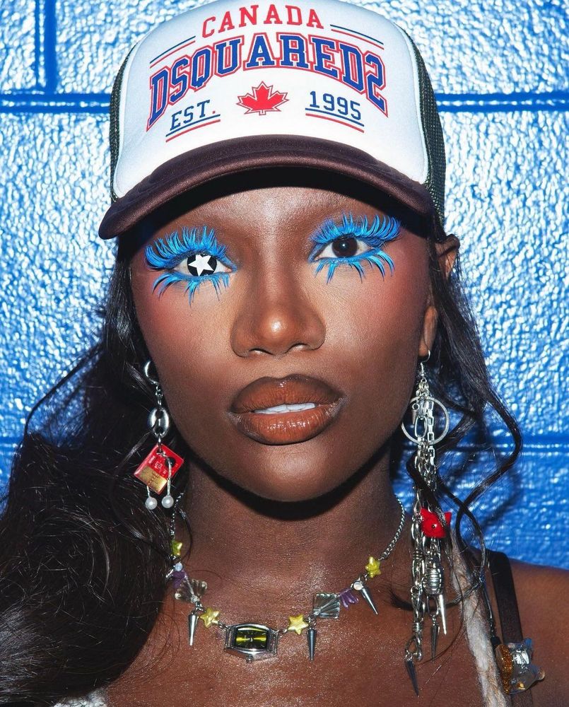 Doechii wearing bright blue eyeliner and lashes, wearing a star shaped contact lense in one eye 