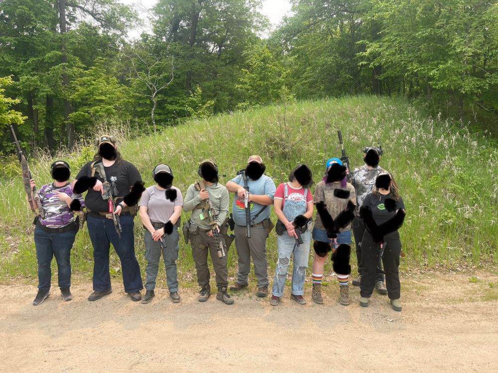 Nine people stand each with a gun or riffle in their hand. 