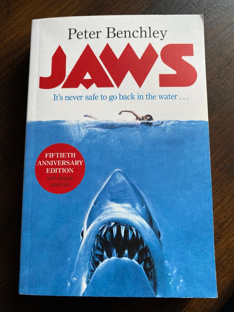 The cover of the 50th anniversary edition of the book Jaws, by Peter Benchley, depicting the upper half of a great white shark surging to the surface towards an unsuspecting female presenting swimmer.