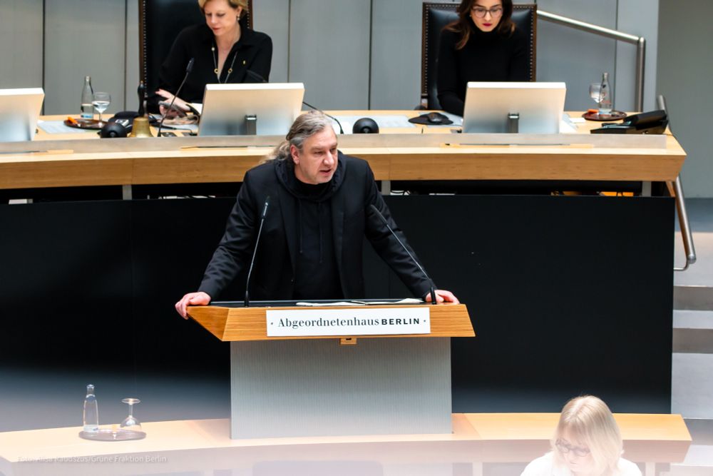 Stefan Taschner steht am Redepult des Abgeordnetenhauses. Er hat beide Hände auf das Pult aufgestützt und hält seine Rede mit ernstem Blick.