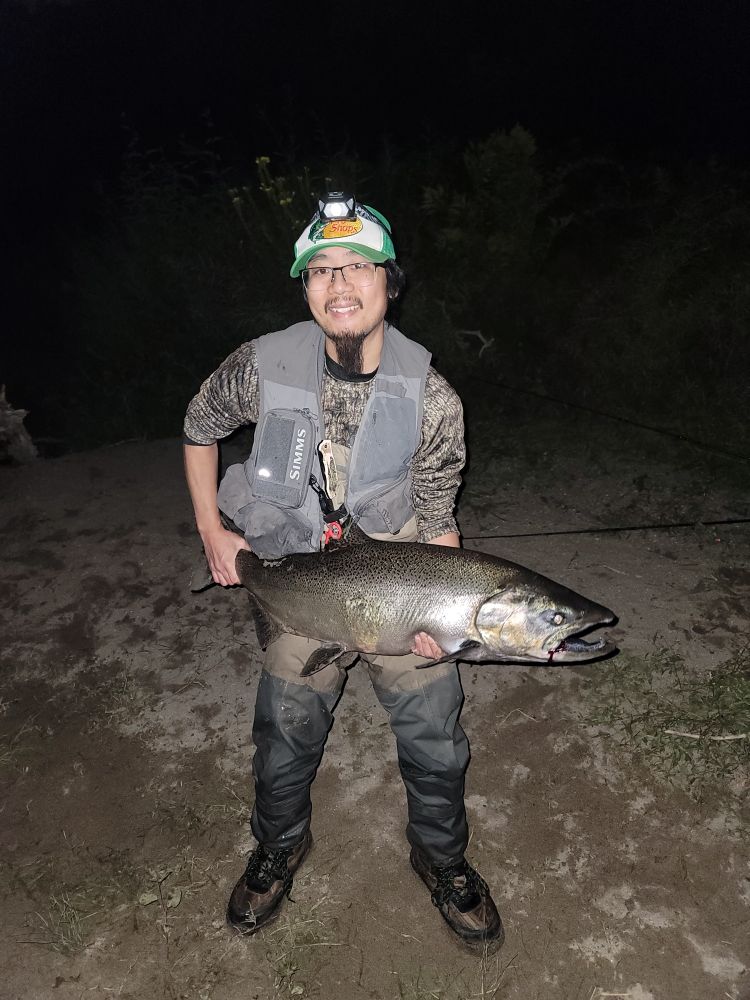 An angler holding up a large male chinook salmon, with its distinctive kype hook jaw visible