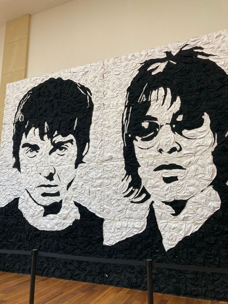 A mixed media portrait of Noel and Liam Gallagher made from black and white bucket hats. 