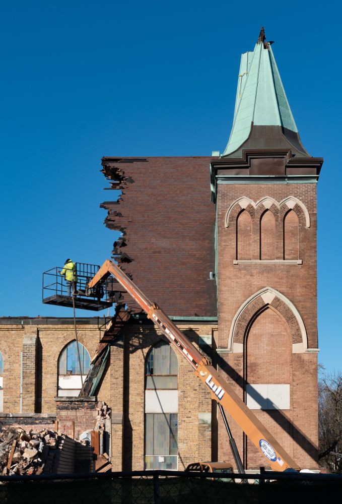 guy in optic yellow on a piece of construction equipment over the half-demolished sanctuary of a church 