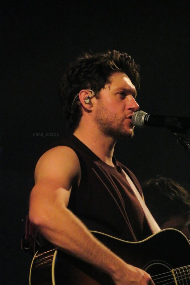 Niall Horan on stage playing guitar and singing into the mic