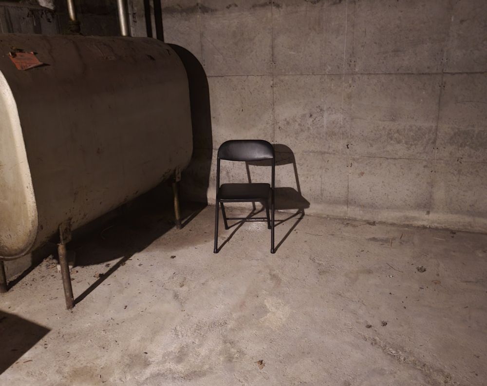 A black chair sitting in the corner of a basement menacingly.