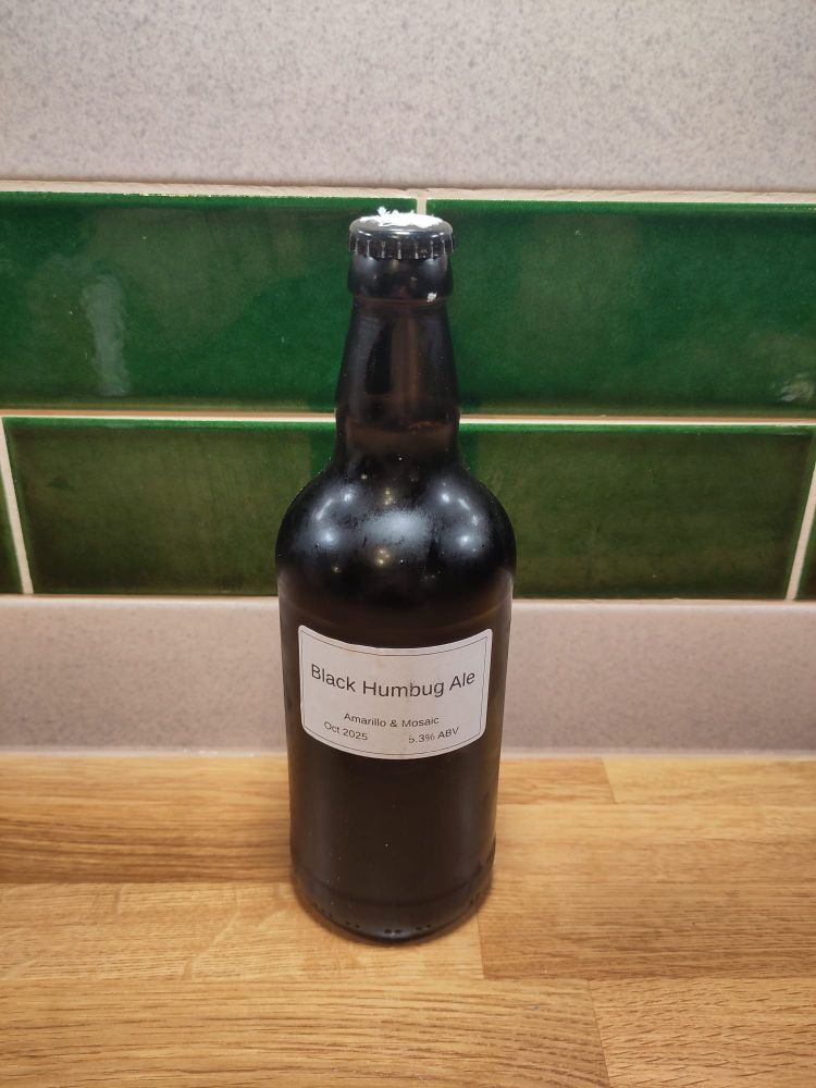 Bottle of "Black Humbug"  stout with a white label in front of green tiles. 