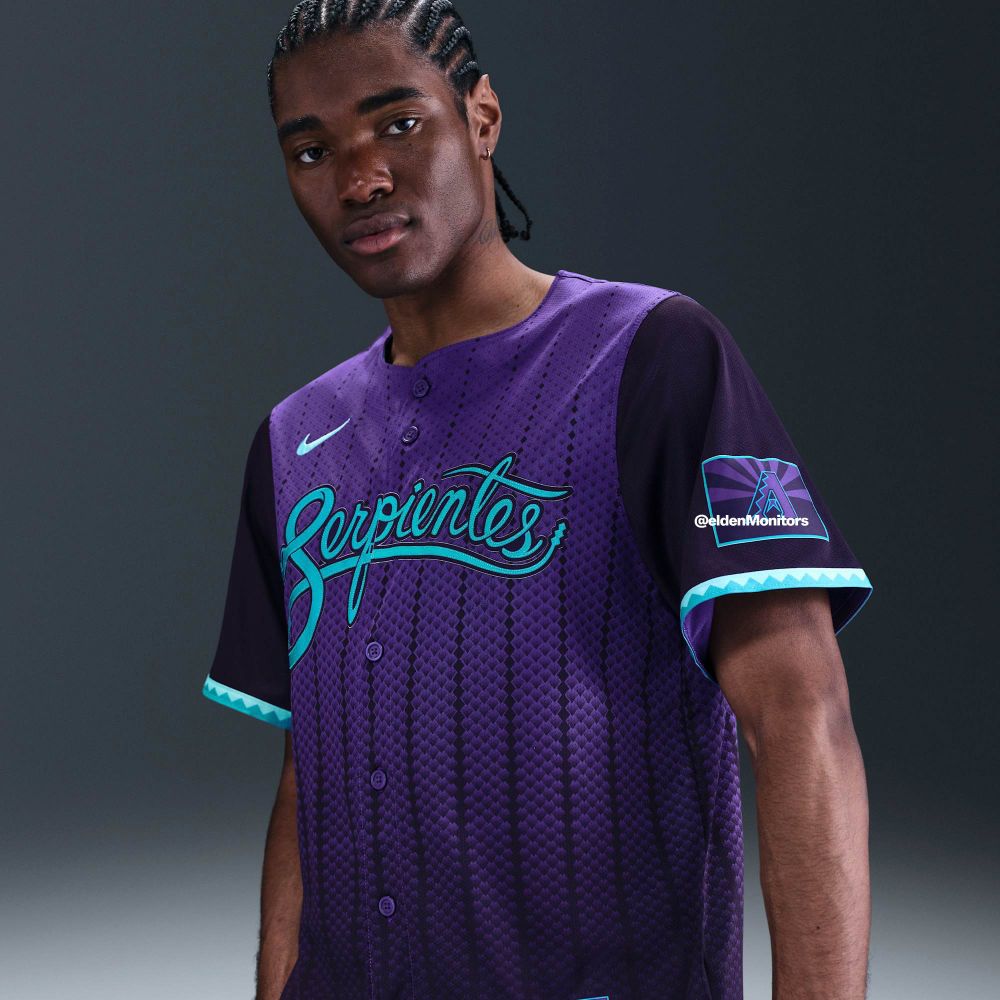 A dark purple baseball jersey with vertical stripes of snake scales that resemble a pinstripe pattern. The torso and sleeves are two different shades of purple to give the torso a vest-like look. On the front of the jersey in teal cursive script is the Diamondback’s previous City Connect “Serpientes” logo.

The sleeves feature a modified Arizona flag that uses two different shades of purple with the star replaced by a purple and teal Diamondbacks “A” logo. The sleeves end with a teal alternating triangle pattern like the profile view of a diamondback rattlesnake’s distinctive scale pattern