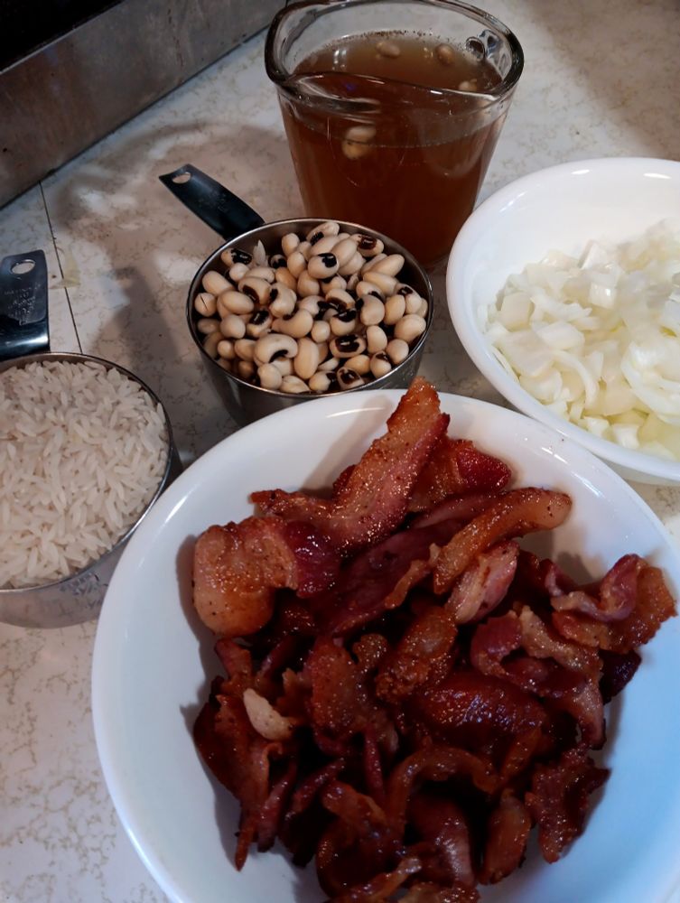 Containers holding rice, like eyed peas, bacon, onions, and pea liquid