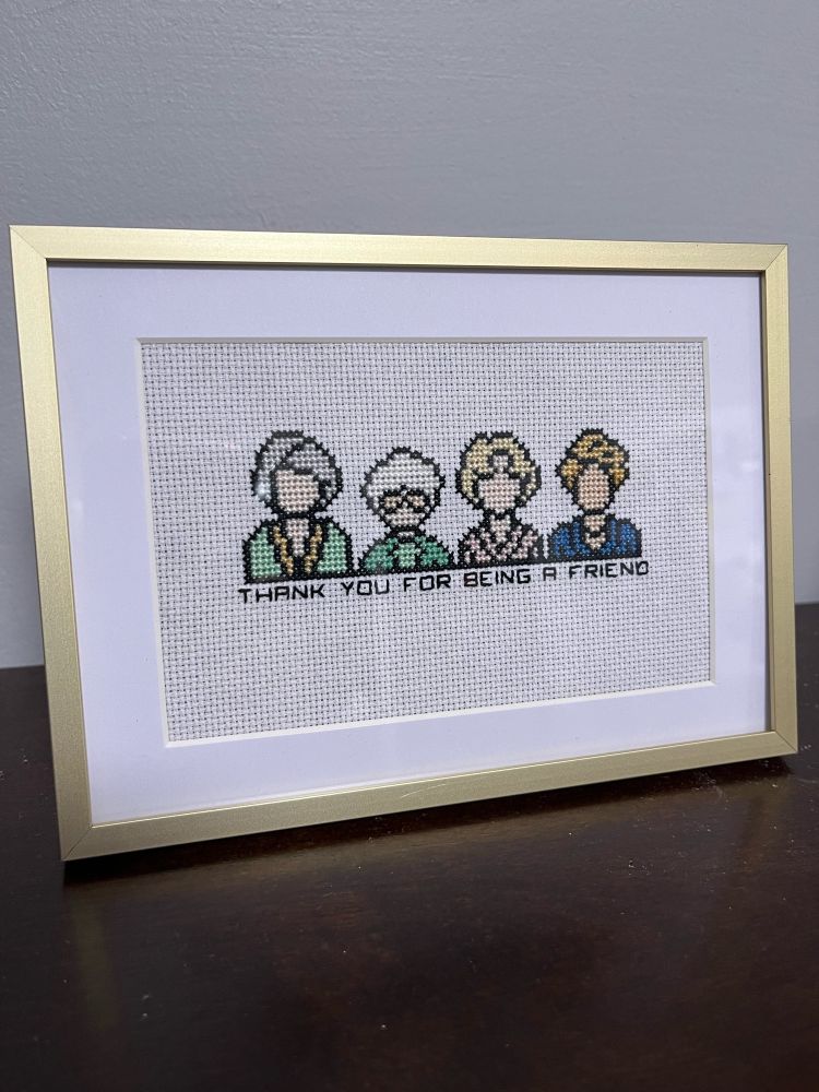 A gold framed cross stitch of the four main characters of the golden girls with the text “thank you for being a friend” underneath. 