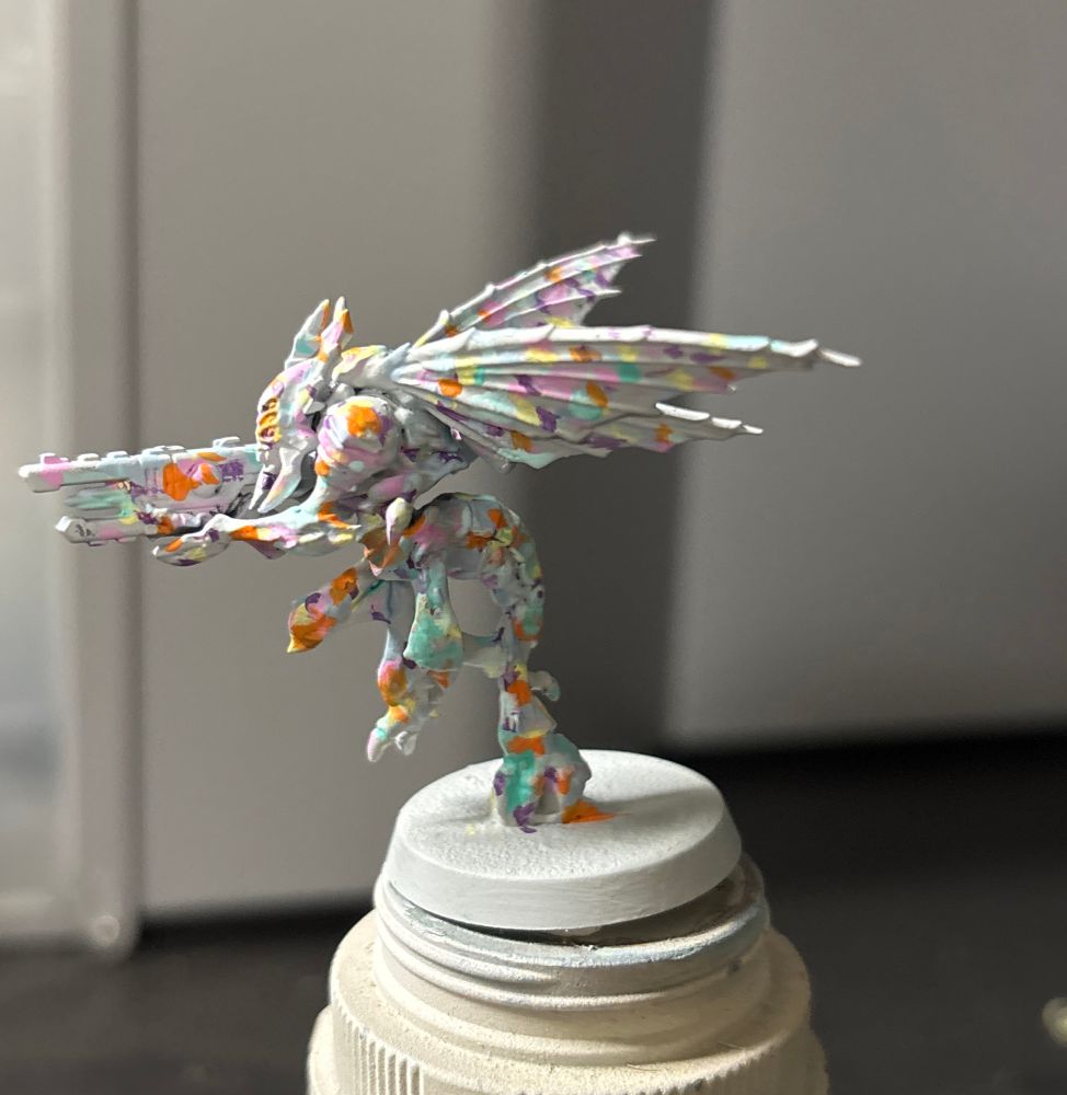 A Vespid Stingwing from a Warhammer Kill Team box, painted Corax White and covered with pastel spots to evoke candy sprinkles or possibly confetti