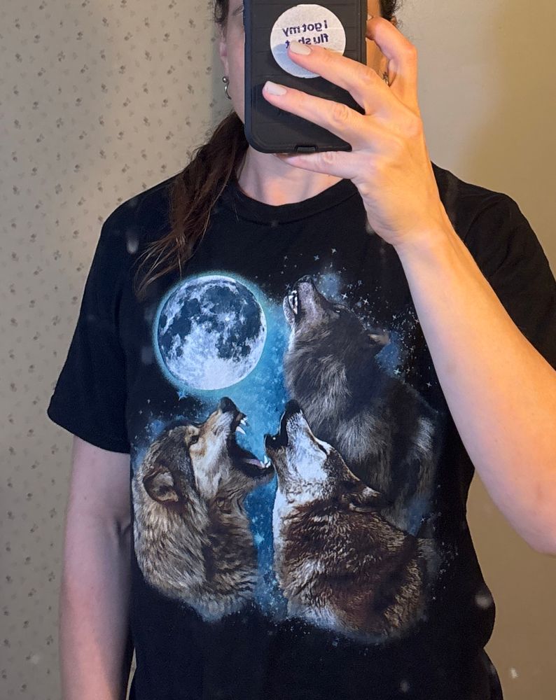 Cropped mirror selfie of a woman wearing the “three wolves howling at the moon” t shirt. You can get one real cheap on Amazon or many other less evil online retailers 