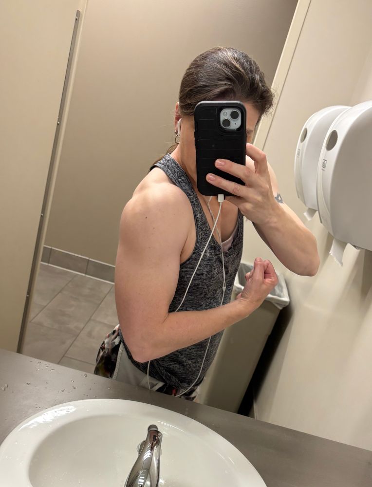 A muscular woman flexing her shoulder in a bathroom mirror