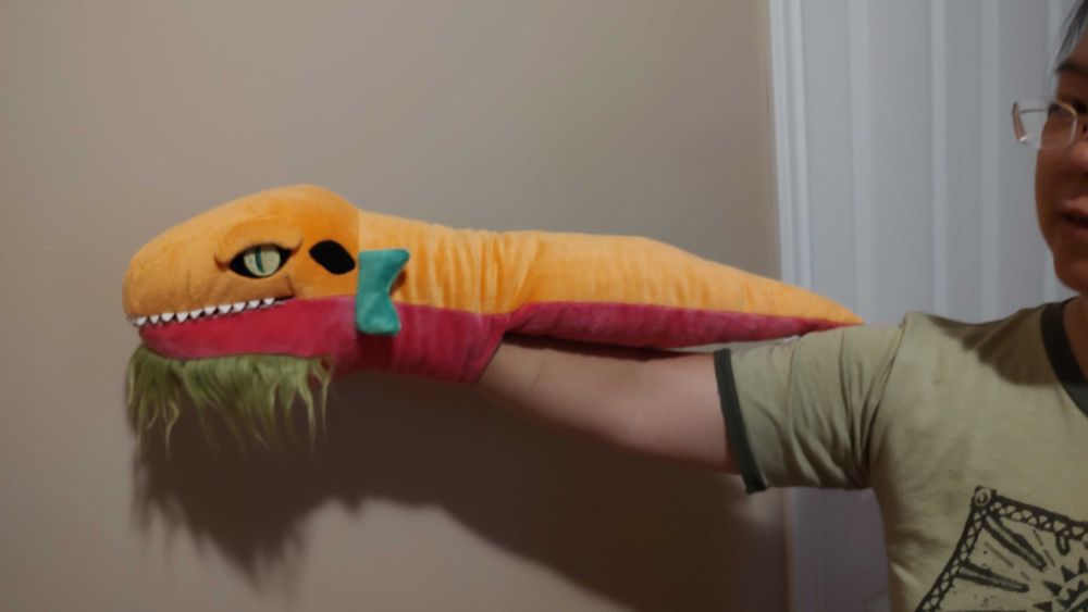 The first prototype of the Jormungandr puppet. He's tropical orange and raspberry red colored. Plus his tail is a stubby little thing. My hand is inserted in a pouch at his neck which allows me to manipulate his mouth.