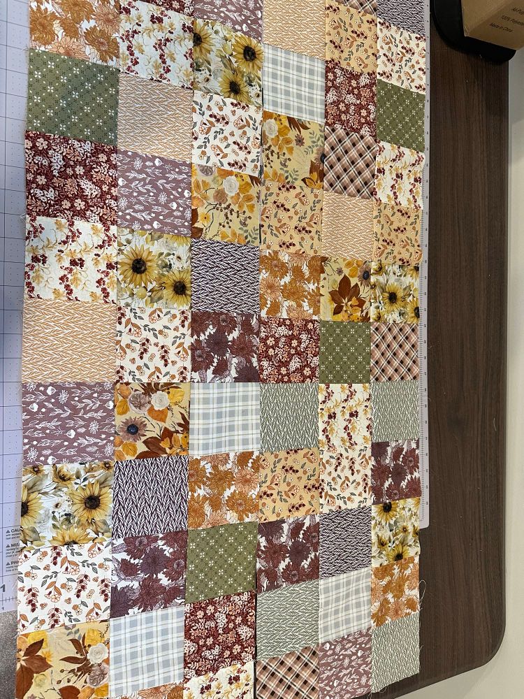 4” squares of fall themed fabric (green, purple, orange) sewed together lying on a table. 