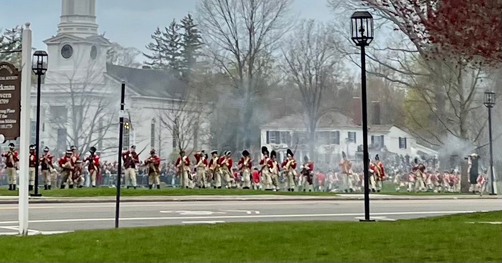 In a reenactment of the Battle of Lexington (1775), gun smoke rises amid the chaos as British regulars and Minutemen exchange musket fire. 
