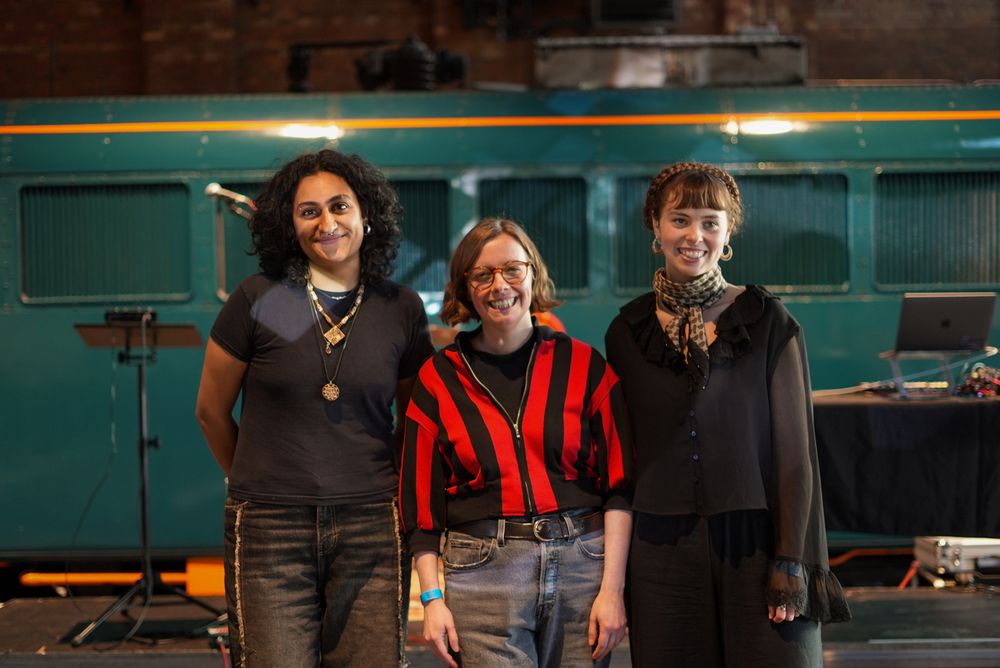 Photo of all three artists standing smiling in front of the train.
Photo by Arya Kokate