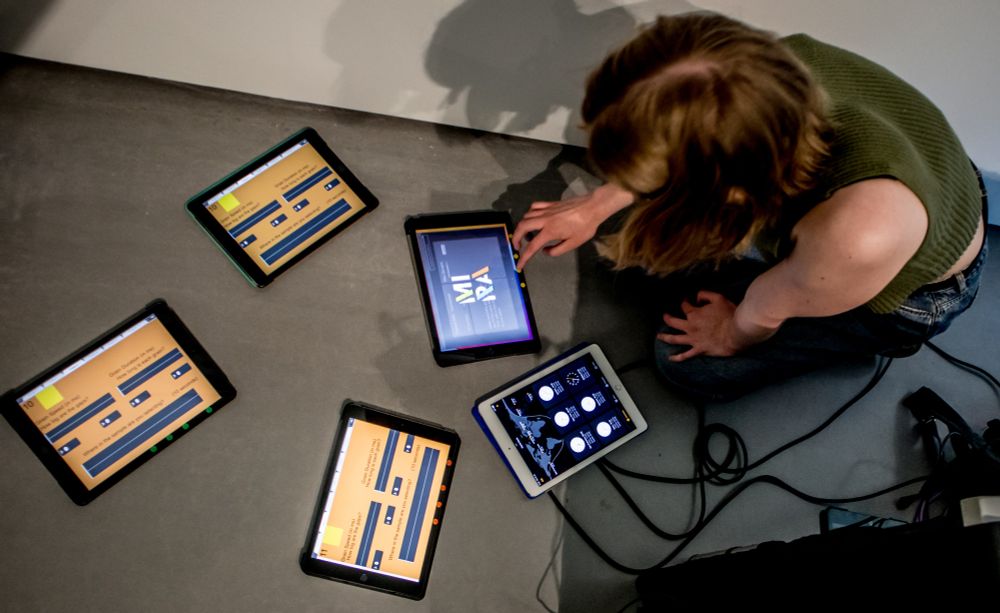 A young woman kneeling in front of several tablet devices running music software on a dark grey floor.