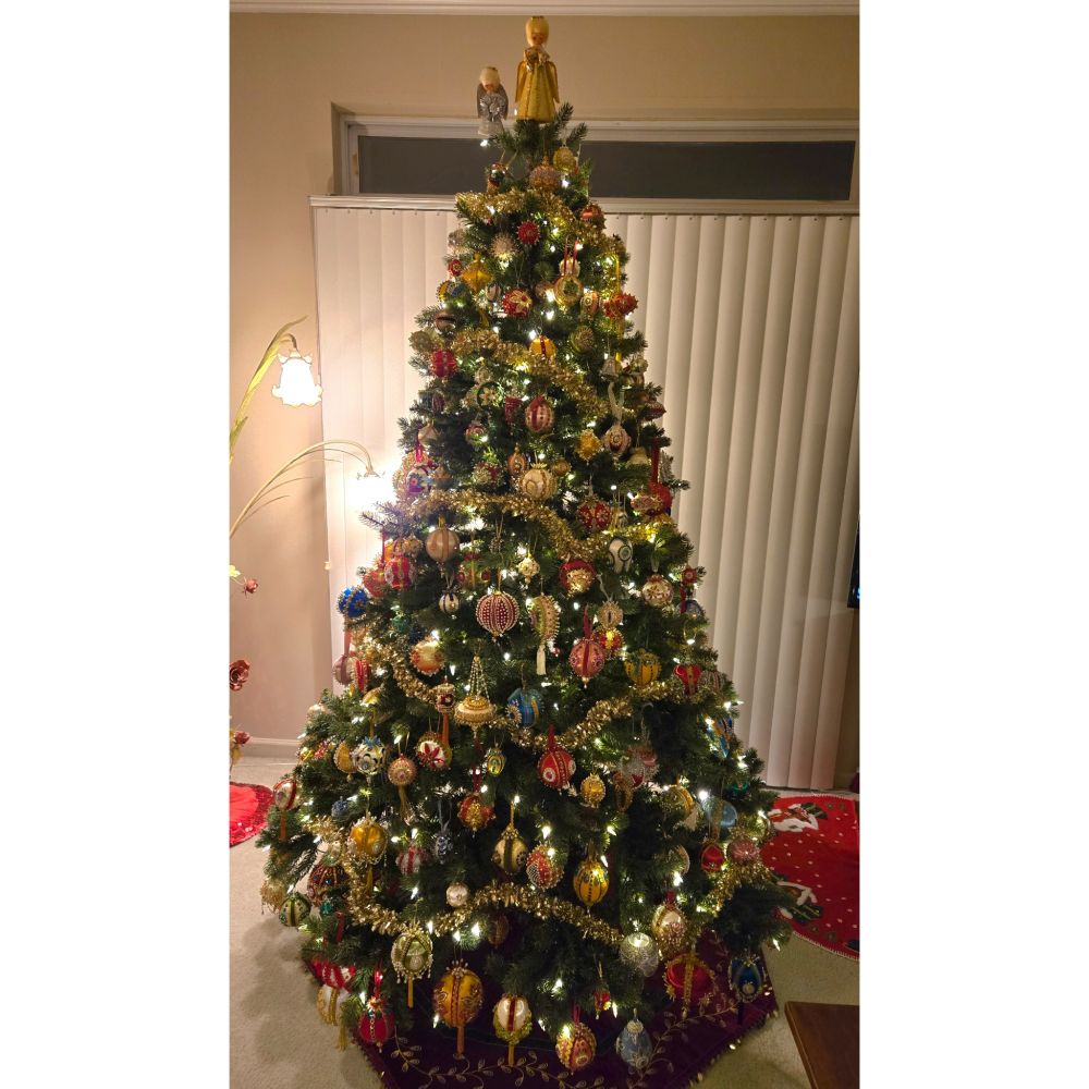 Christmas tree with gold Garland, a gold angel and a smaller silver angel on top, and full of beaded sequin ornaments