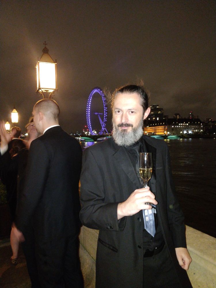 Me with a glass of champagne looking dashing and handsome stood on the terrace of Parliament with the London Eye in the background.