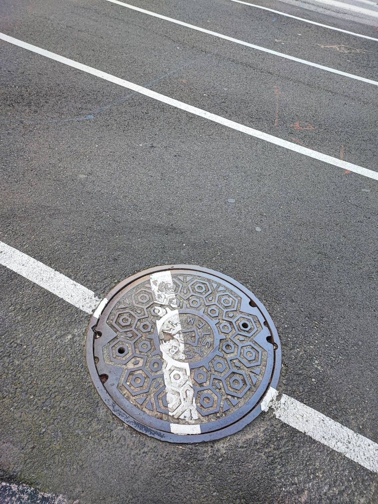 A photo of a man hole cover, where the painted parking line is NOT aligned with the road painted line...