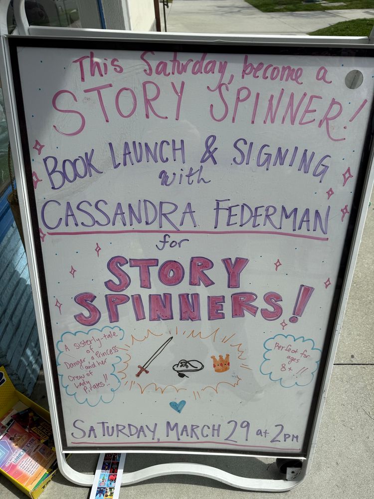 An easel outside the bookstore reads this Saturday become a story, spinner book launch and signing with Cassandra Federman for story spinners