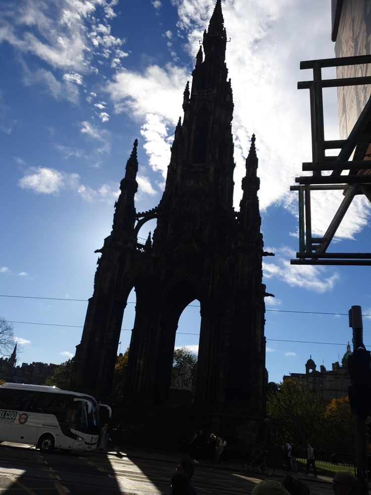 OK, wow.

This is the Walter Scott monument in East Prince's Street Gardens, Edinburgh, silhouetted against a bright blue sky. And it's enormous.

It looks like a Gothic cathedral, and when I say Gothic, I'm talking about the Germanic people who built impressive cathedrals, not chicas who like skulls and ravens. There are four arches formed by four pillars, each topped with a spire and crusted with all sorts of embellishments.

Those four pillars support a massive central pillar, held up by flying buttresses. The central pillar rises stepwise; the corners of each layer have their own small spires, and the very top layer culminates in a truly massive spire. Throughout the structure are all sorts of decorative arches carved into the stonework.

On a plinth in the center sits a statue of Walter Scott. The statue is literally larger than life, yet is still dwarfed by the monument around it.