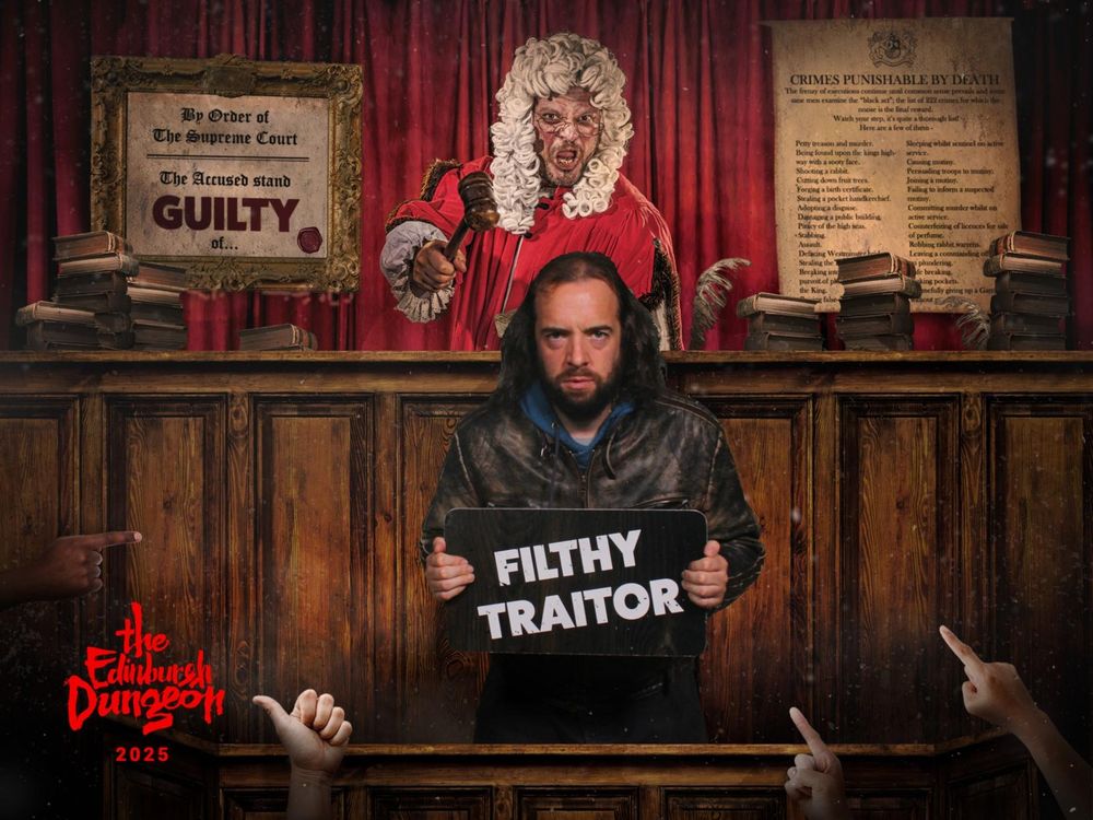 A courtroom.

In the midground stands Infrapink. He is a 39-year-old white man with unruly, shoulder-length hair and a short beard. Here, he us wearing a leather jacket. He has an expression of sullen defiance as he holds up a sign that says "Filthy Traitor".

In the background, a judge wields a gavel. To the judge's right is a sign that says " By order of the Supreme Court, the Accused stands guilty of..."

In the foreground, one hand gives a thumbs up and two others point accusingly at Infrapink.