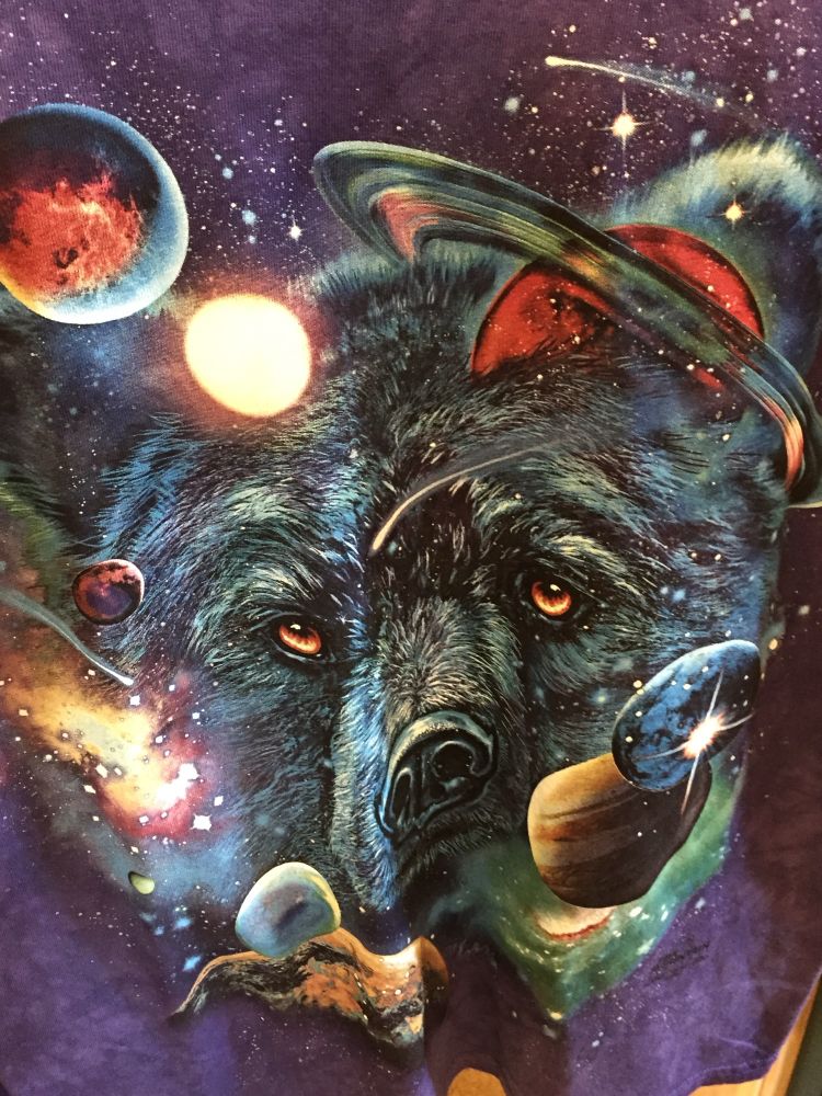A close up of a black t-shirt featuring the head of a black bear surrounded by planets and stars.