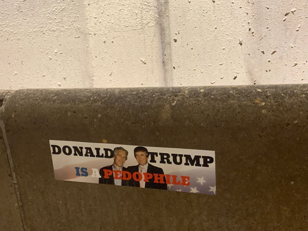 A picture of a bumper sticker on the walls of a DC metro station, showing a picture of Trump and Epstein and the words Donald Trump is a Pedophile.  