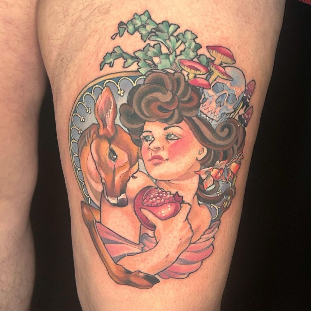 Thigh tattoo of Persephone, surrounded by her symbols- pomegranate, deer, fern, skull- and art nouveau details, in mostly blues pinks and browns 