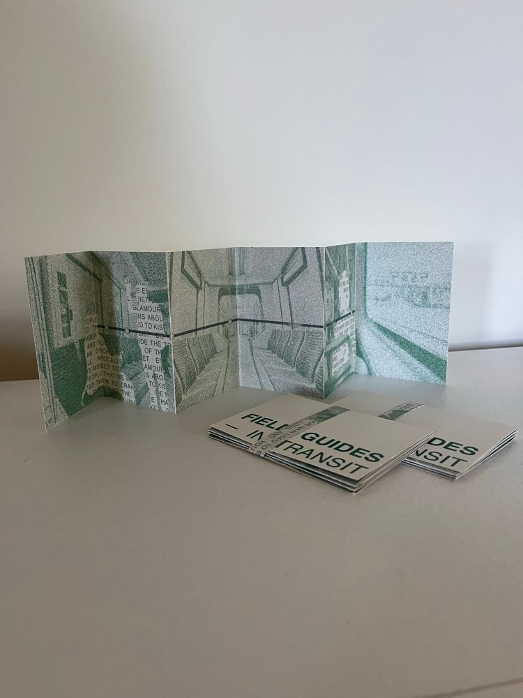 A photo of the Field Guides in transit zine. One copy of the zine is opened accordion style on a white table and two more are folded and flat in front of it. 