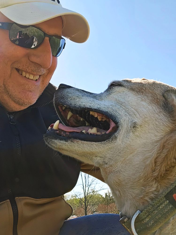 A dog owner kneels down and his dog smiles back at him