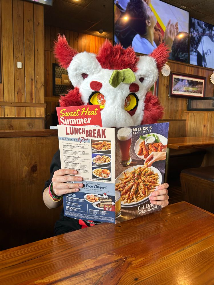 Me in my white and red fursuit head with a sprout on it holding up a menu at a restaurant 