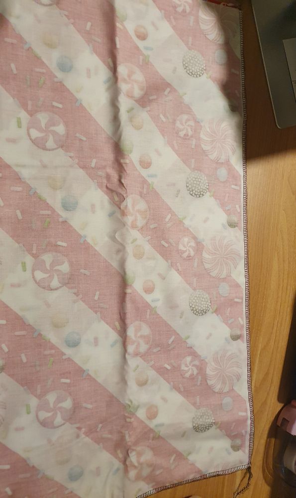 Man sieht einen weihnachtlichen Stoff der auf die linke Seite gedreht ist, die eine Seite ist die Falzkante, zwei andere Seiten sind mit einer Overlocknaht geschlossen.