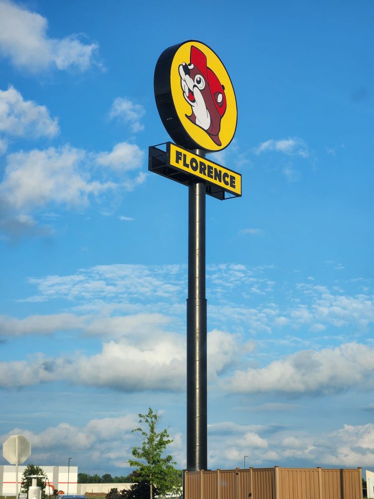 Picture from the parking lot beneath it of the Buc-ee's sign for the Florence (SC) location against a lightly-clouded bright evening sky. 