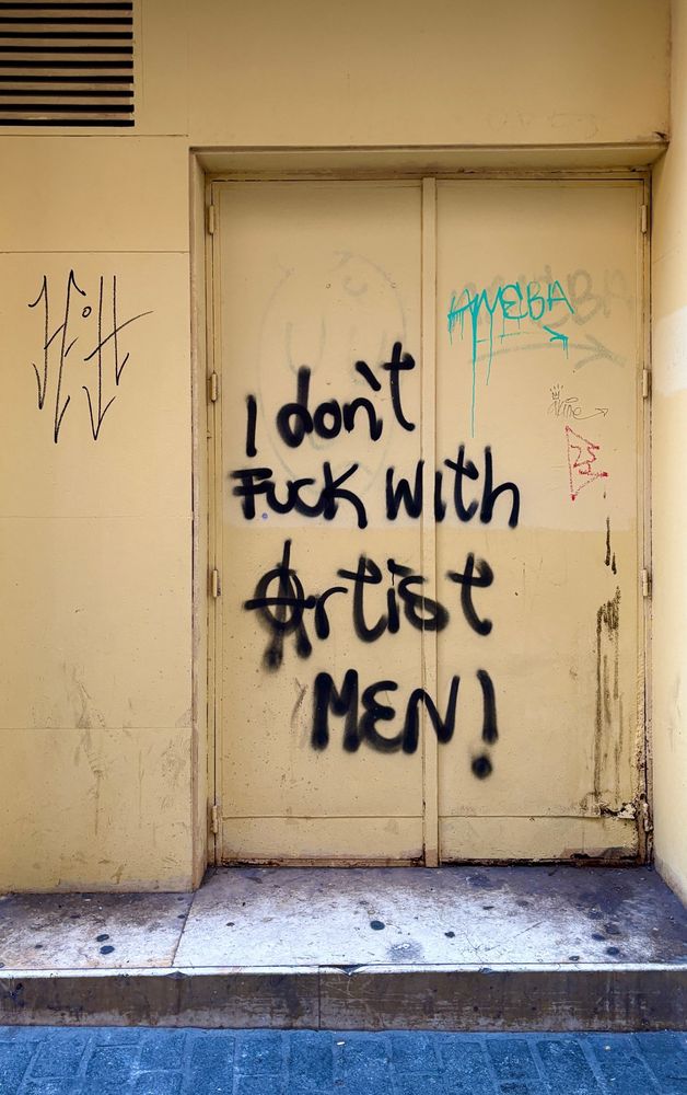 black sprayed graffiti on a yellow metal door, saying “I don’t fuck with artist men!”