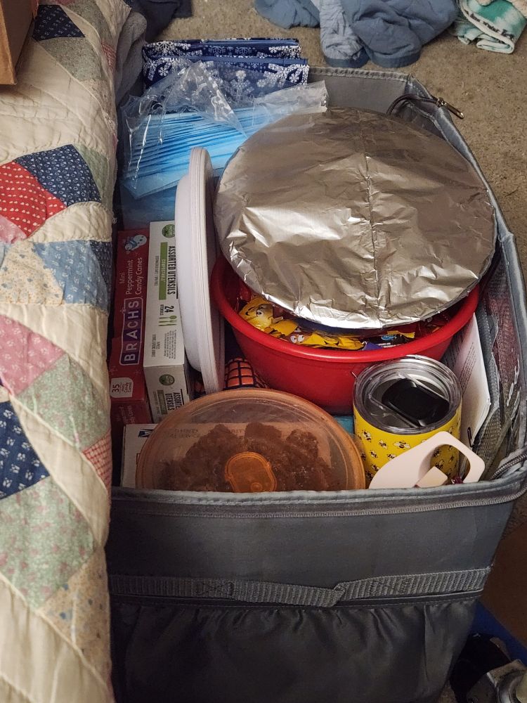 A box of stuff including a tinfoil wrapped plate, Tupperware with cookies, paper plates, and plastic utensils. 