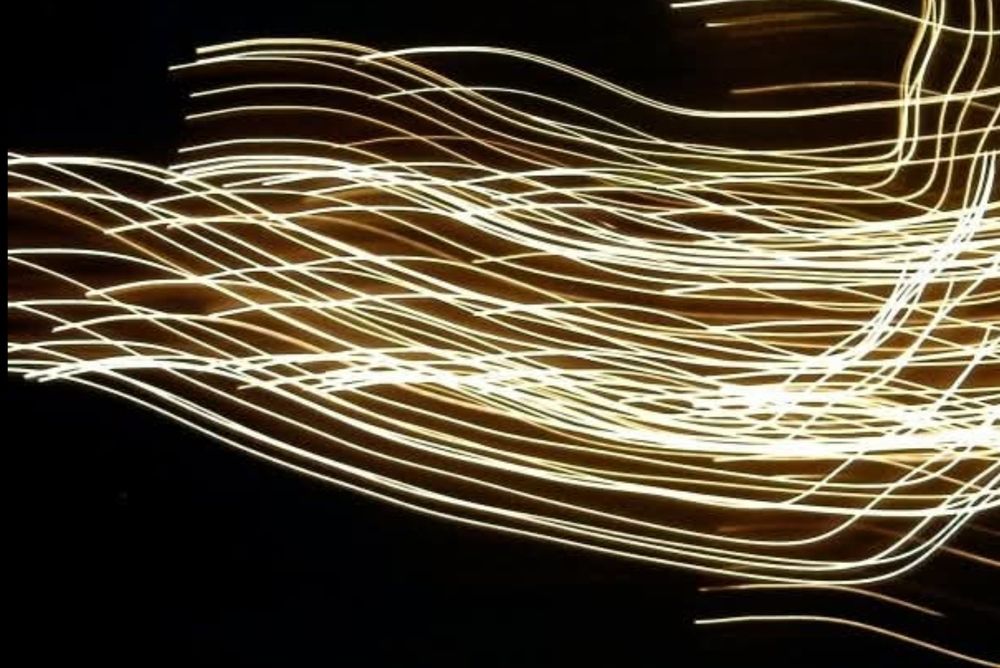 The photo depicts abstract light trails created through long-exposure photography. The image displays characteristics of ICM (Intentional Camera Movement), where the camera is moved during a long exposure to create streaks and patterns of light, often resulting in abstract or ethereal effects. The image showcases a dynamic interplay of bright, wavy lines, suggesting motion and energy.  The image's focus on simple forms (lines of light) and a limited color palette (light lines on a dark background) aligns with the core principles of minimalism, which emphasizes simplicity, reduction, and the absence of superfluous elements.
