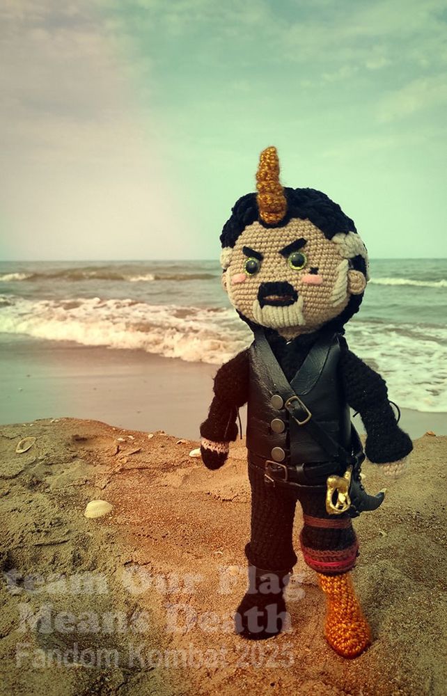Plushie Izzy by team OFMD from Fandom Kombat. He's at the beach, his expression is displeased. He has a tiny sword, unicorn horn and his wooden leg.