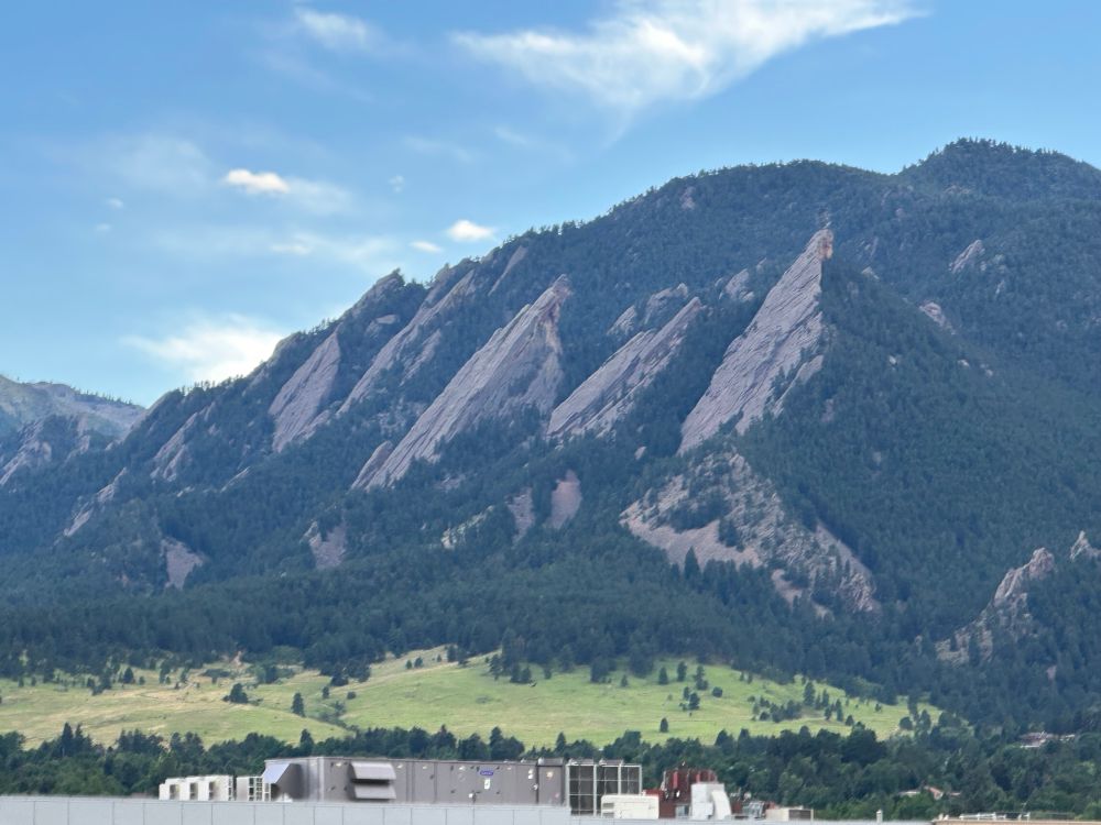 Bite from a roof top bar in Boulder with green hills giving way to trees and mountains behind.  