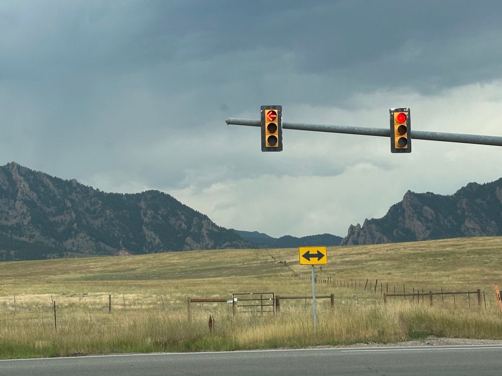 A fork in a road where across the street is a foothold to the Rocky Mountains. 