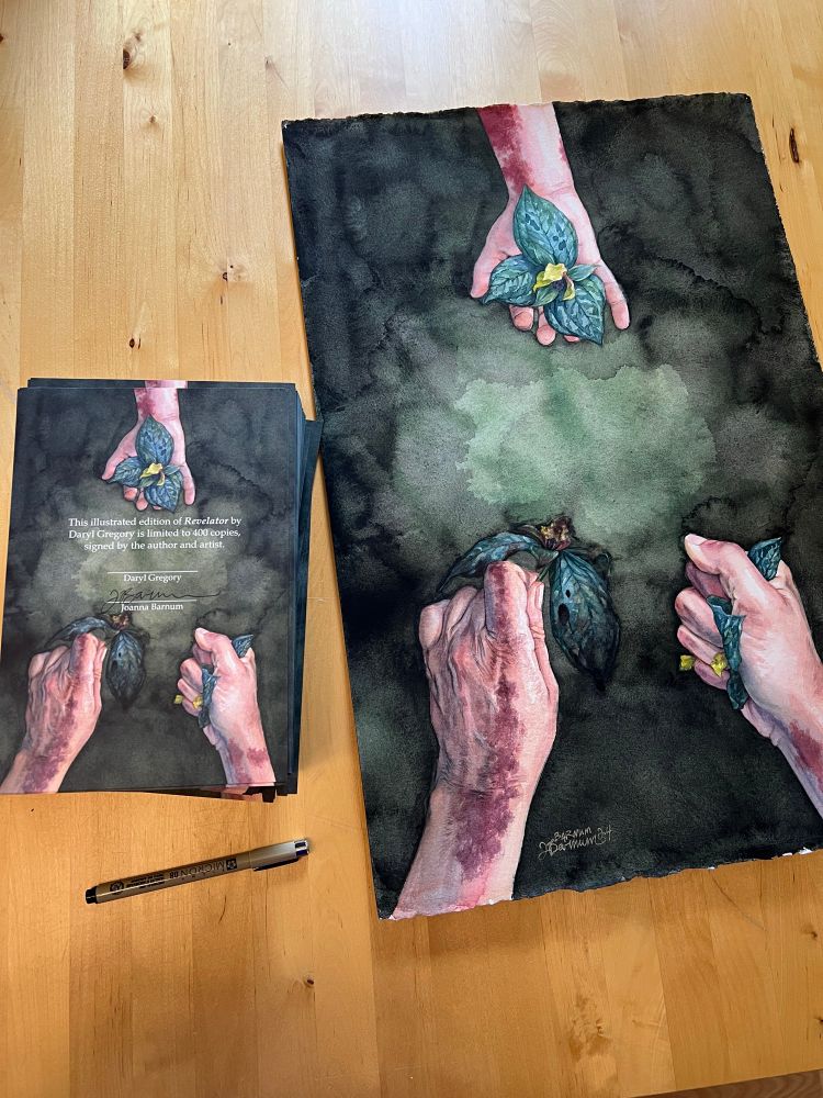 Photo of the signature pages sitting next to a much larger original watercolor painting of the same art 